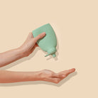 Hand holding a green silicone cup against a beige background