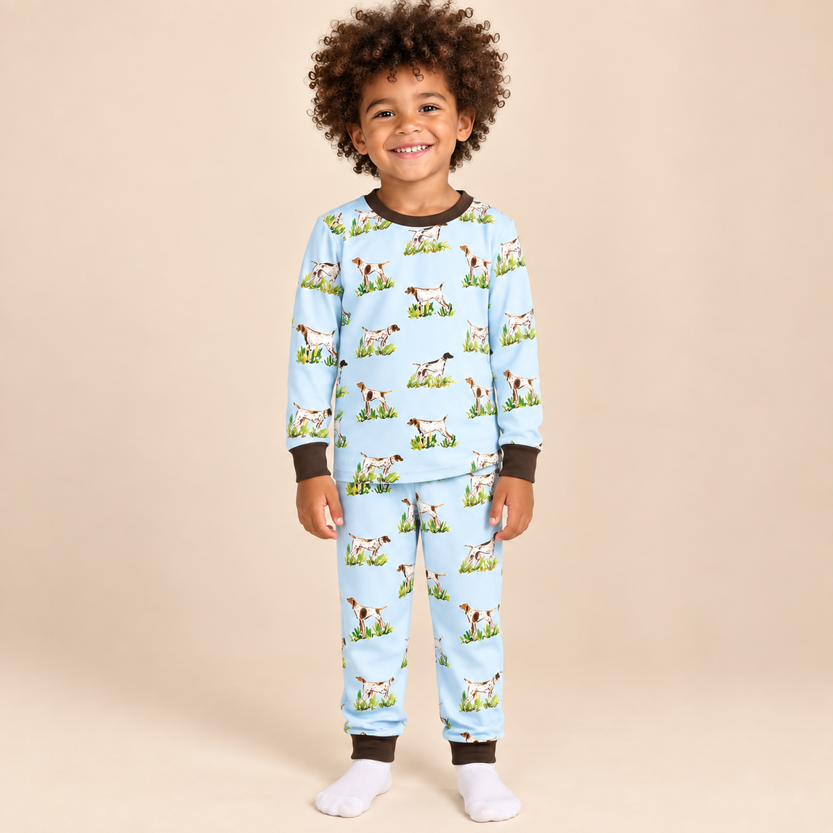Boy wearing a light blue bird dog print bamboo lounge set with long sleeves, matching pants, and dark brown neckline and cuffs.
