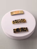 Three hair clips with leopard print pattern on a round white stand.