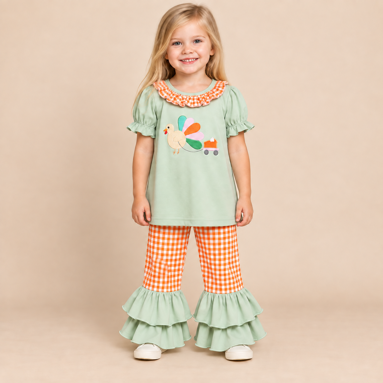 Toddler girl wearing a sage turkey embroidered shirt with orange and white gingham pants.