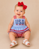 Baby wearing a blue outfit with 'USA' print and red checkered details on a beige background