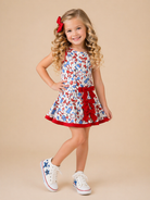 Young girl wearing a patriotic dress with red trim and white sneakers on a beige background
