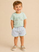 Child wearing a mint green t-shirt with a car design and striped shorts on a beige background
