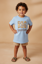 Boy standing with a blue BIG BROTHER embroidery shirt on beige background.