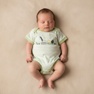 Newborn wearing a green striped romper on beige background.