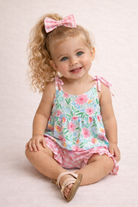 Young girl wearing a floral dress with a pink bow on a light pink background