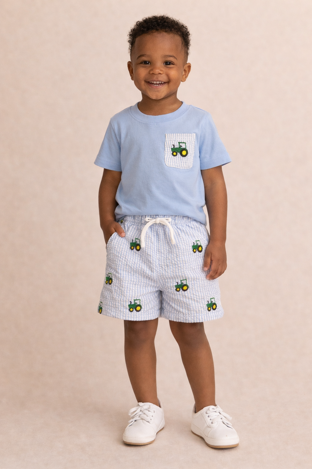 Child wearing a light blue t-shirt and shorts with tractor patterns on a beige background