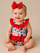 Baby wearing a floral swim suit with red ruffled collar and matching headband on a beige background