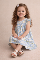 Young girl wearing a floral dress sitting on a beige background