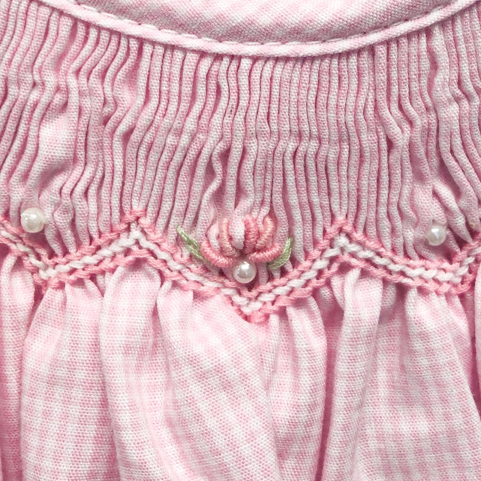 Close-up of a pink textured fabric with floral embroidery and pearl embellishments.