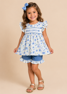 Young girl wearing a floral dress with 'Jesus Loves Me' text on a beige background