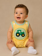 Baby wearing a yellow bubble with a green tractor design on a beige background