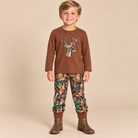 Young boy wearing a brown long sleeve shirt with an embroidered camo deer and matching camo pants.