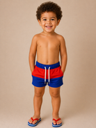 Toddler boy wearing red and blue swim trunks.