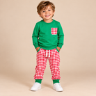 Toddler boy wearing a long sleeve green shirt and red & white gingham pants.