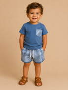 Child wearing a blue shirt with a pocket and checkered shorts on a beige background