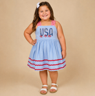 Young girl wearing a USA blue dress with red ric rak on the bottom. 