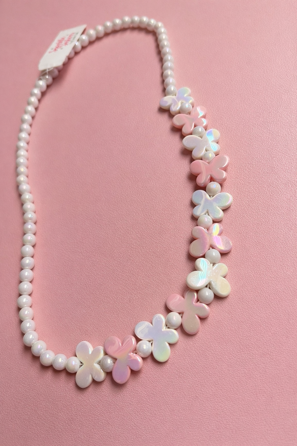 Necklace with white pearls and flower-shaped beads on a pink background