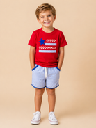 Child wearing a red t-shirt with a blue star and white stripes, paired with blue shorts on a beige background