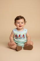 Baby wearing a light blue romper with sailboat design on a beige background