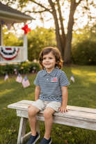 Boy in navy stripe polo sitting on white picket fence, patriotic summer setting
