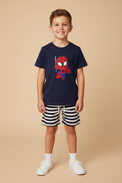 5 year old boy wearing navy graphic embroidered tee and navy white striped shorts with white sneakers on beige background