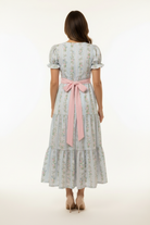 Woman wearing a floral dress with a pink belt on a white background