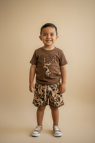 Child wearing a brown t-shirt with a graphic and patterned shorts on a beige background
