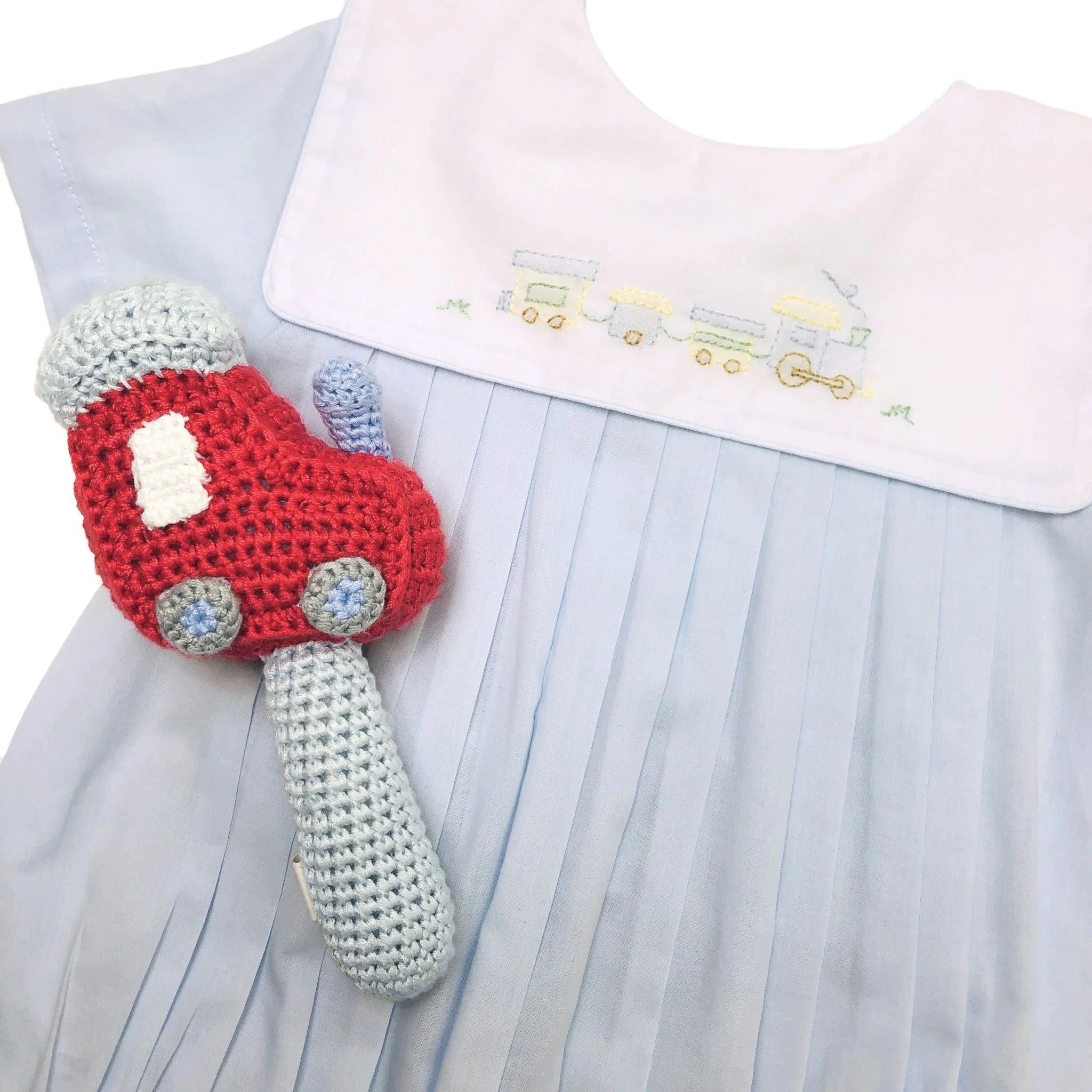 Crocheted toy car held by a child wearing a light blue dress with embroidered details.
