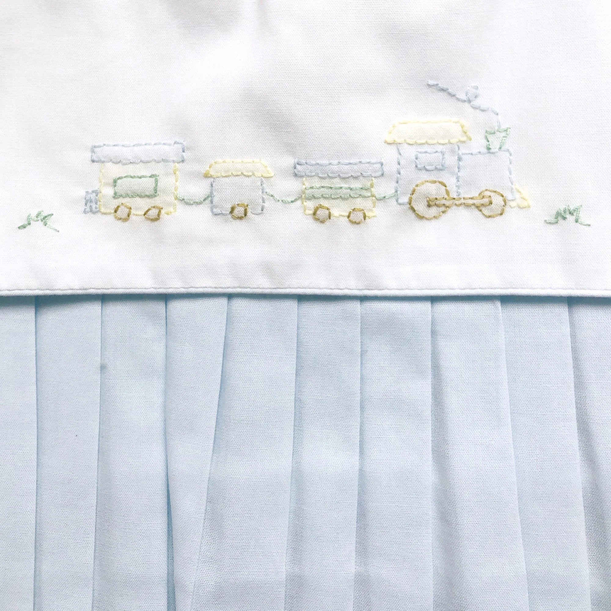 Embroidered train design on a white fabric with a light blue tulle overlay.