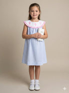 Young girl wearing a light blue dress with a white collar holding a white book on a beige background