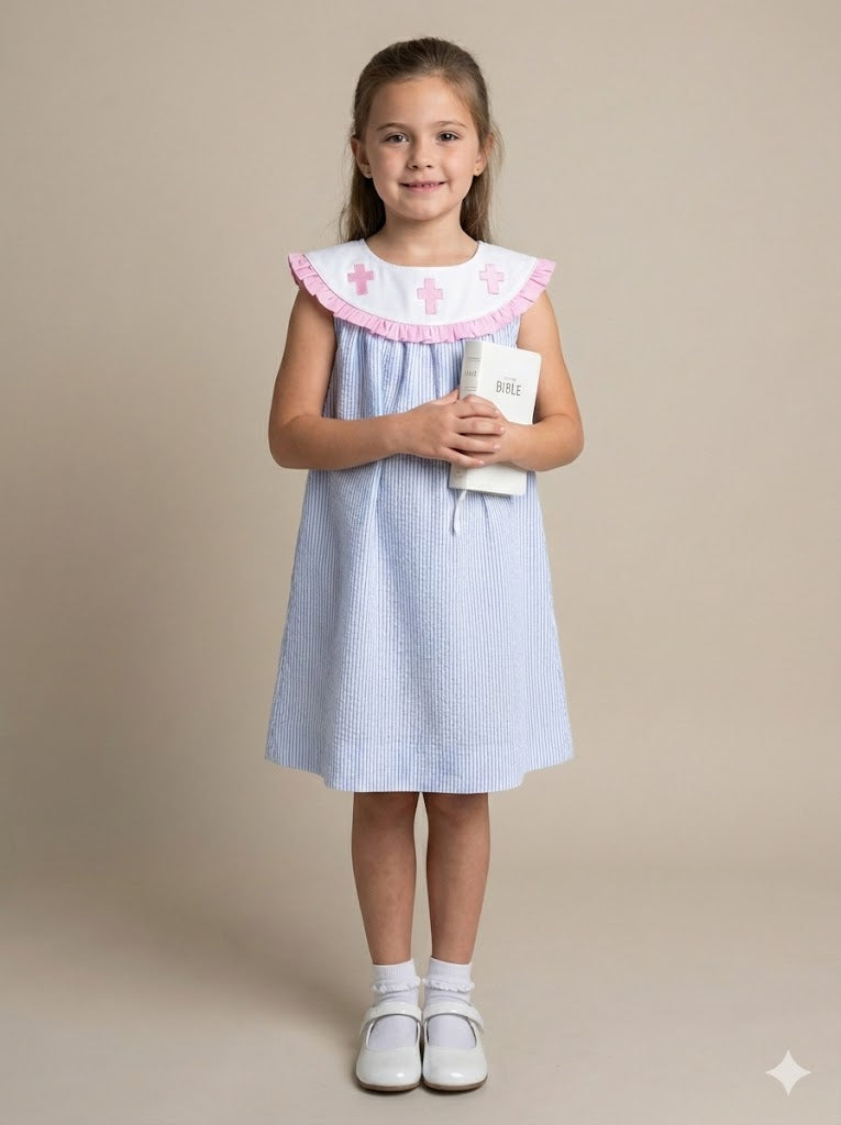 Young girl wearing a light blue dress with a white collar holding a white book on a beige background