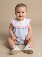 Baby wearing a light blue dress with pink ruffled collar and cross details on a beige background