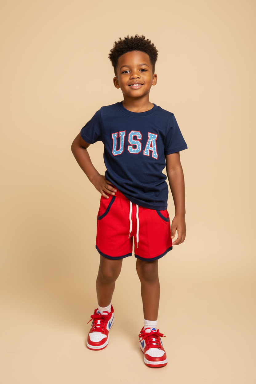 Boy wearing a navy shirt that says USA with red shorts.