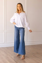 A woman wearing a white balloon-sleeve blouse with jeans, standing indoors.